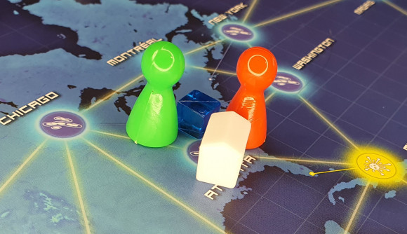 Two colored pawns, a white research centre, and a single disease cube on the city of Atlanta in the board game Pandemic