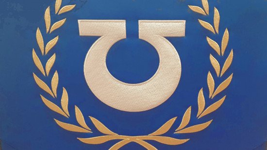 The embroidered logo of the Ultramarines, a white inverted Omega symbol, in a gold wreath, on the blue leatherette surface of the Warhamemr 40k gaming chair